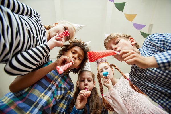 Low angle view at group of happy kids blowing party horns at camera and having fun